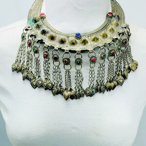 Può includere: Una collana d'argento con un grande ciondolo decorato e catene pendenti con ciondoli a forma di cuore. Il ciondolo è decorato con piccole pietre colorate.