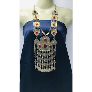 May include: A long gold necklace with a large ornate pendant featuring red and blue stones. The pendant has a fringe of small gold chains and drops.