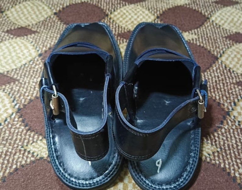 May include: A pair of black leather sandals with a strap and buckle. The sandals have a blue stitching detail around the edges.