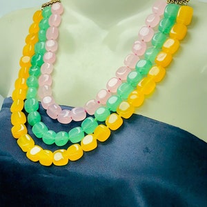 May include: A three-strand necklace made of yellow, green, and pink gemstone beads. The beads are faceted and have a polished finish.