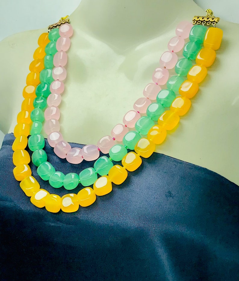May include: A three-strand necklace made of yellow, green, and pink gemstone beads. The beads are faceted and have a polished finish.