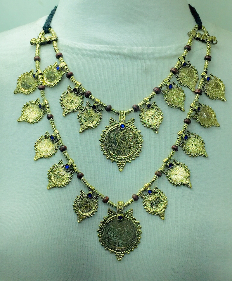 May include: A gold necklace with multiple round pendants and blue accents. The necklace is made of wood beads and metal.