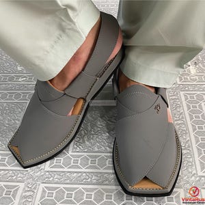 K&ouml;nnte beinhalten: Graue Ledersandalen mit quadratischer Zehenpartie und Ziern&auml;hten. Die Sandalen haben ein einzigartiges Design mit &uuml;berlappenden Riemen und einem kleinen Logo. Die Sohlen sind schwarz, getragen mit hellgr&uuml;ner Hose.