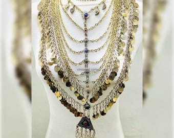 May include: A multi-layered gold-toned necklace with coin and chain details. The necklace features various gemstone accents and a triangular pendant with dangling chains. The necklace is displayed on a white mannequin.