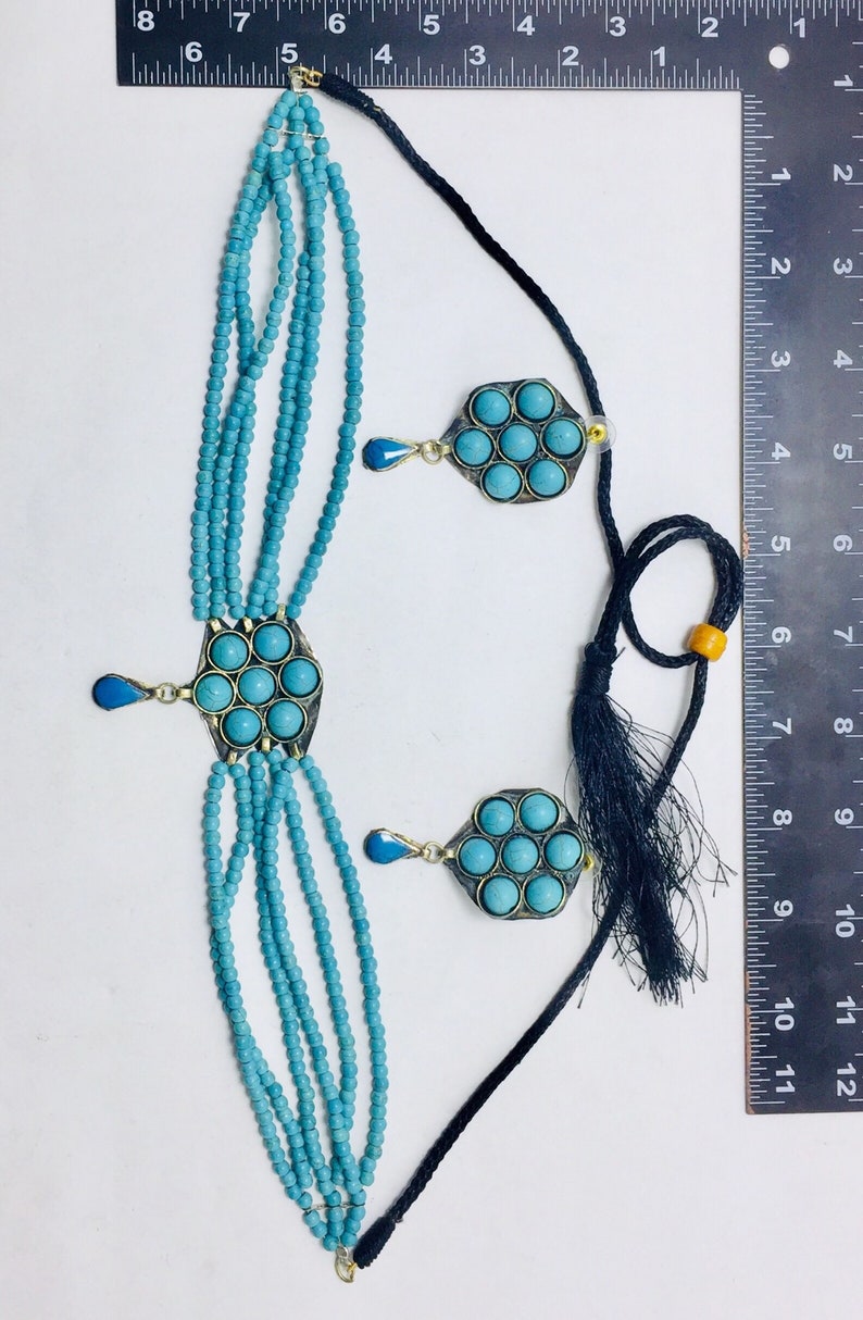 May include: A turquoise blue beaded necklace with two pendants featuring turquoise stones set in silver. The necklace is on a white background with a ruler for scale.