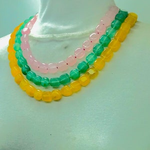 May include: A layered necklace with three strands of beads. The top strand is pink, the middle strand is green, and the bottom strand is yellow.