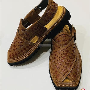 May include: A pair of brown leather sandals with a woven design. The sandals have a black sole and a strap that goes around the ankle. The sandals are handmade.