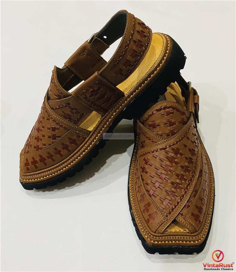 May include: A pair of brown leather sandals with a woven design. The sandals have a black sole and a strap that goes around the ankle. The sandals are handmade.
