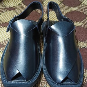 May include: A pair of black leather sandals with a strap and buckle. The sandals have a pointed toe and a flat sole.