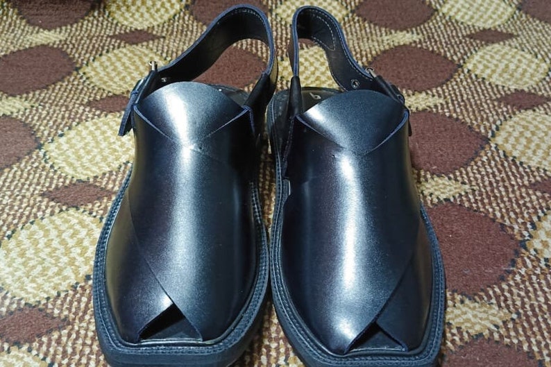 May include: A pair of black leather sandals with a strap and buckle. The sandals have a pointed toe and a flat sole.