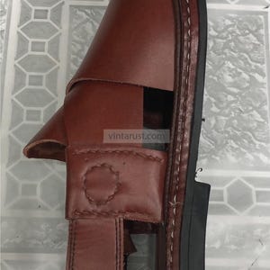 Puede incluir: Sandalia de cuero marr&oacute;n con correa y cierre de hebilla. La sandalia tiene una suela cosida y una base de goma negra. La marca "VintaRust Handmade Classics" es visible en la esquina inferior derecha.