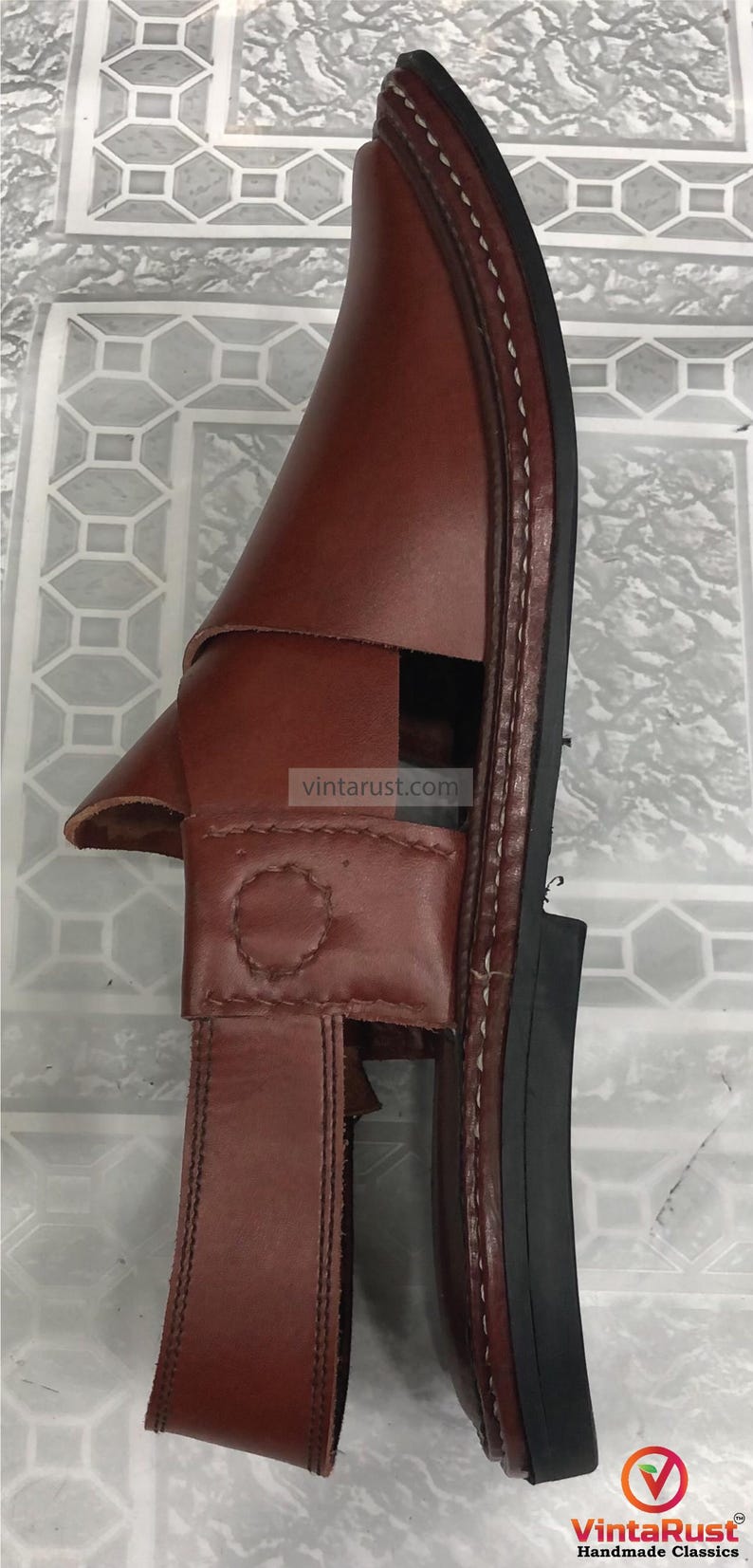 Puede incluir: Sandalia de cuero marr&oacute;n con correa y cierre de hebilla. La sandalia tiene una suela cosida y una base de goma negra. La marca "VintaRust Handmade Classics" es visible en la esquina inferior derecha.
