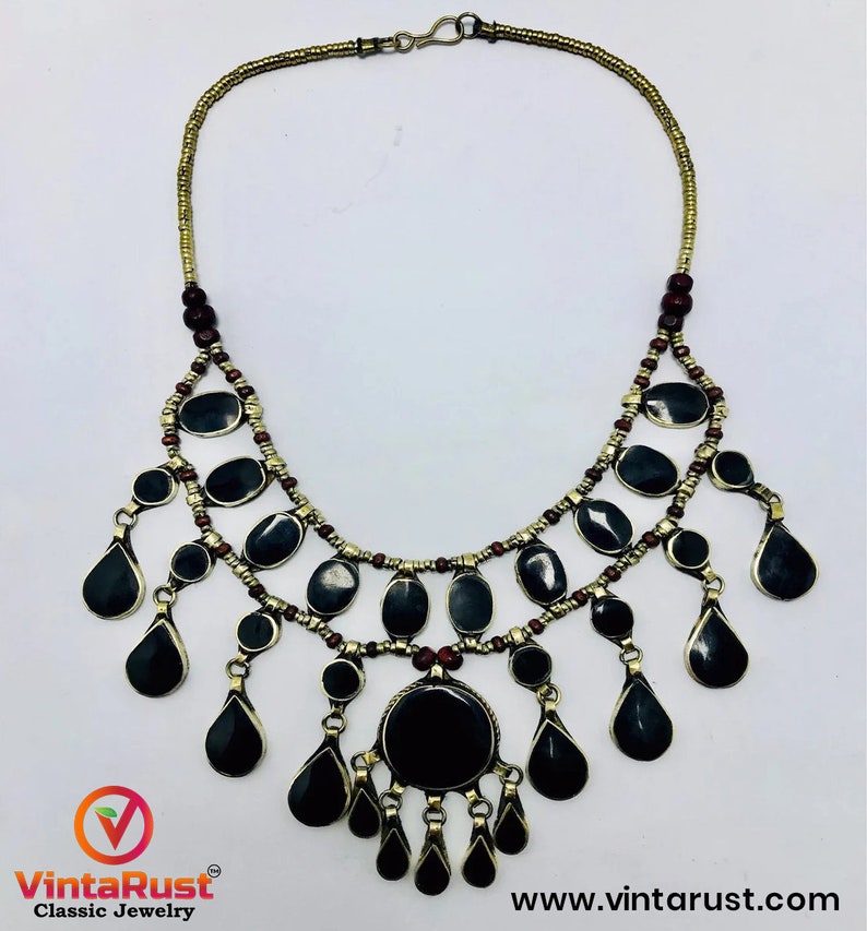 Pode incluir: Um colar preto e dourado com um grande pingente preto e v&aacute;rios pingentes pretos menores. O colar &eacute; feito de contas de metal e tem um fecho.