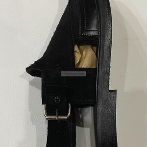 May include: Black leather sandal with a suede vamp and a buckle closure. The sandal has a thick sole and a minimalist design. The image also shows the website vintarust.com.