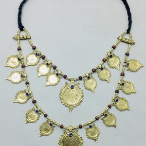 May include: A gold necklace with a double strand of brown beads and gold coin-shaped pendants. The pendants have blue gemstones in the centre. The necklace is tied with a black cord.