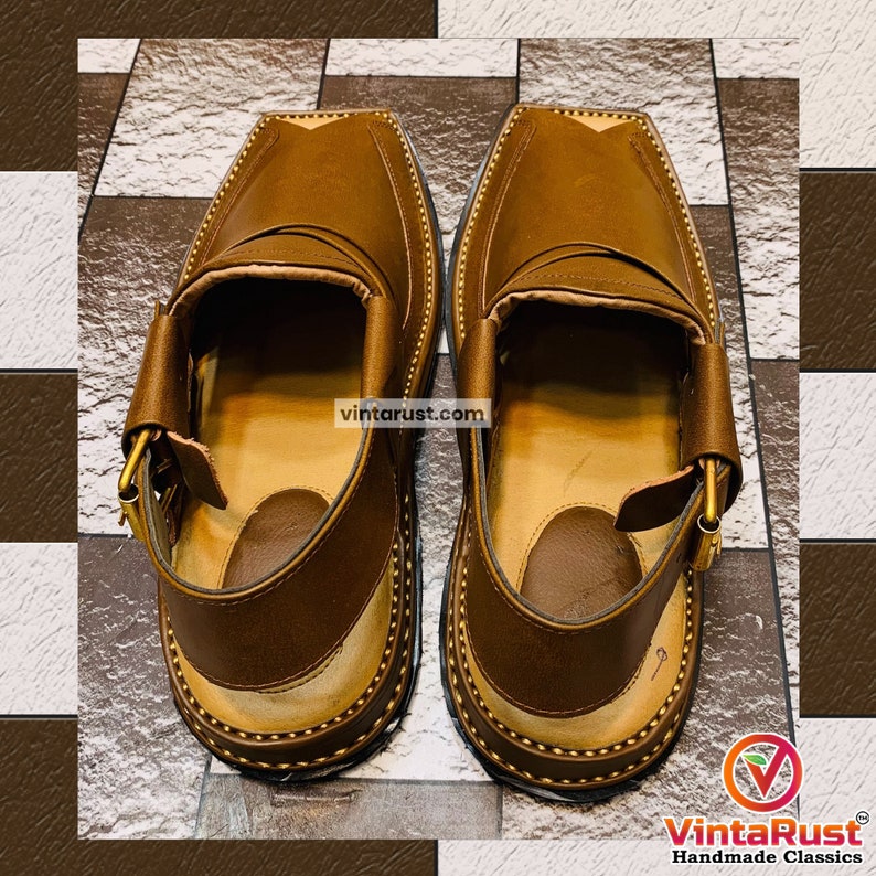 K&ouml;nnte beinhalten: Ein Paar braune Ledersandalen mit einem Schnallenriemen. Die Sandalen haben einen gen&auml;hten Rand und eine braune Ledersohle.
