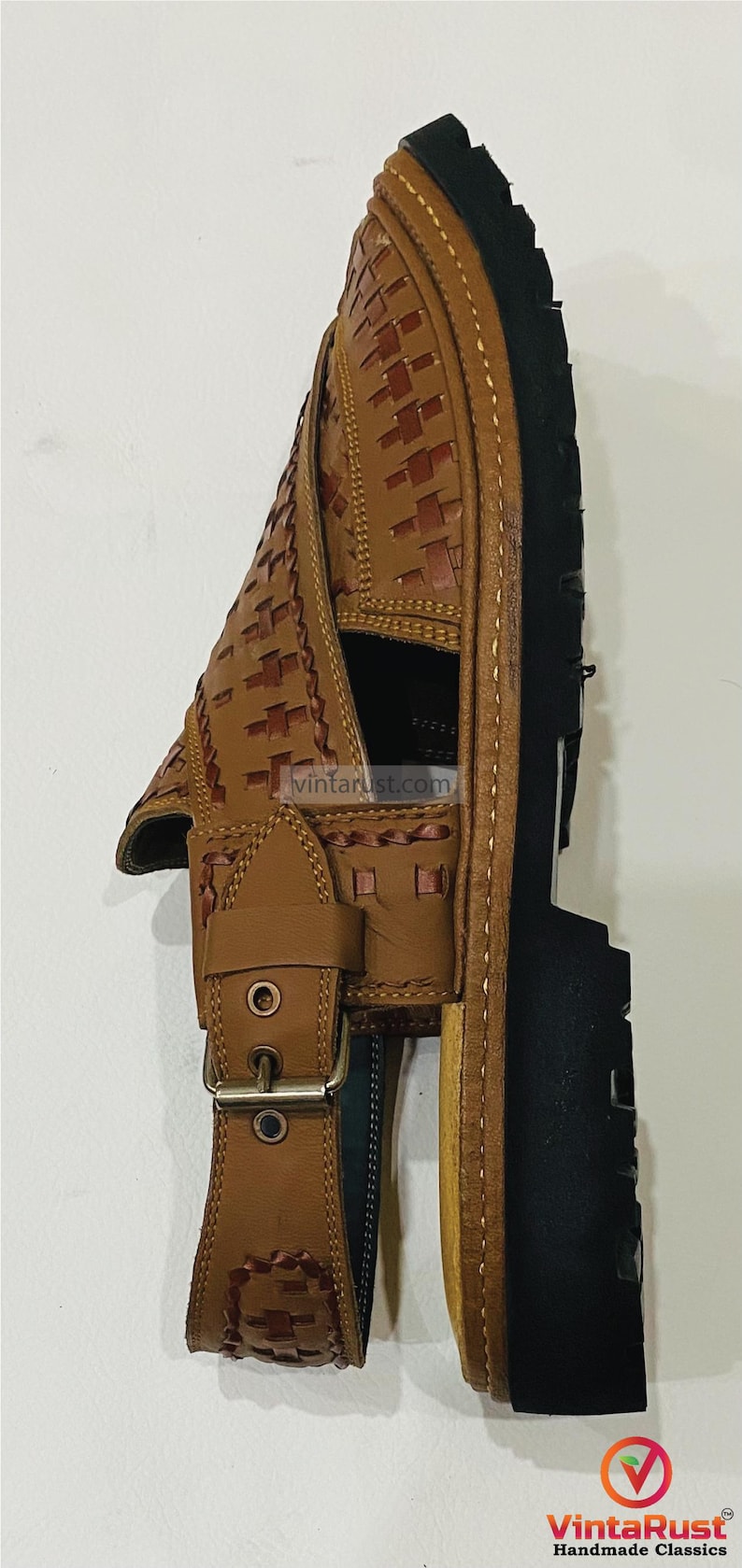 May include: Brown leather sandal with a woven design on the upper and a black sole. The sandal has a buckle closure and is handmade. The brand name "VintaRust" is visible.