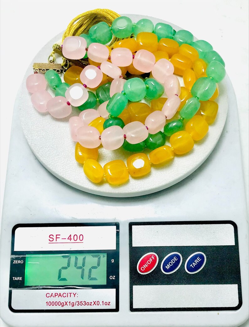 May include: A close-up of a digital scale displaying 242 grams. Three strands of beads are on the scale, one strand is yellow, one is green, and one is pink.
