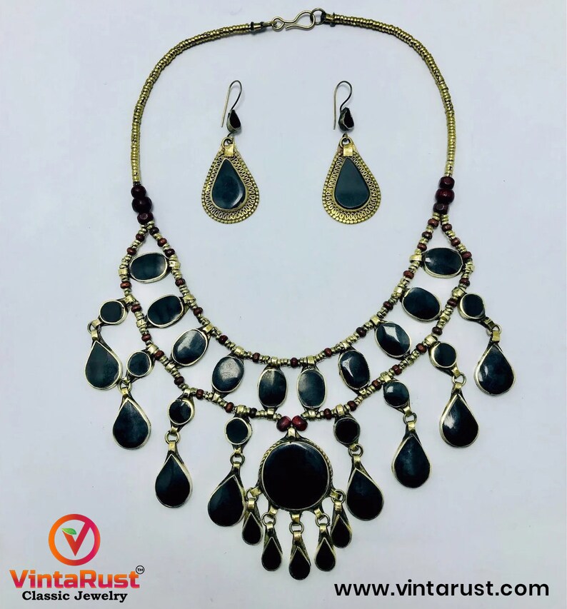 Pode incluir: Um colar preto e dourado com um design de l&aacute;grima e brincos combinando. O colar tem v&aacute;rias camadas de contas e pingentes em forma de l&aacute;grima. Os brincos s&atilde;o formas simples de l&aacute;grima com pedras pretas.