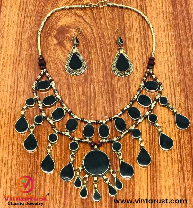 Pode incluir: Um colar de ouro com contas pretas e marrons e um grande pingente preto. O colar &eacute; acompanhado por um par de brincos combinando com pedras pretas em forma de l&aacute;grima.