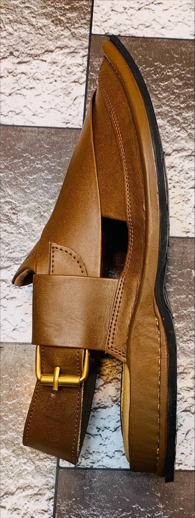 K&ouml;nnte beinhalten: Braune Ledersandalen mit Schnallenverschluss und schwarzer Gummisohle.