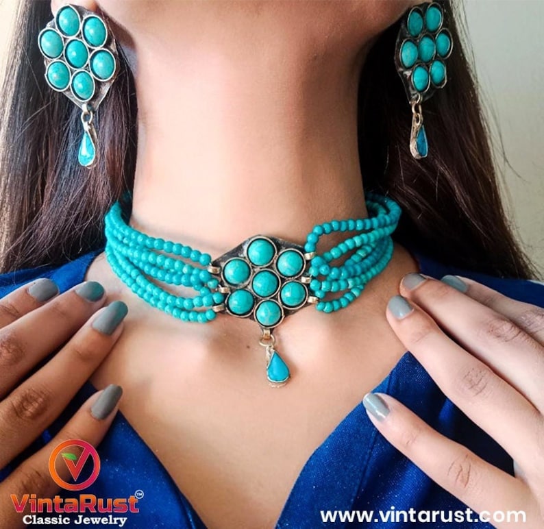 May include: A turquoise blue beaded choker necklace with a large turquoise pendant. The necklace has a silver-tone metal base and is layered with multiple strands of beads. Matching turquoise earrings with a silver-tone metal base are also included.