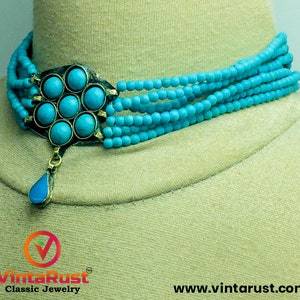 May include: A turquoise blue multi-strand beaded choker necklace with a large turquoise stone pendant. The pendant is a flower shape with a teardrop-shaped stone hanging from the center.