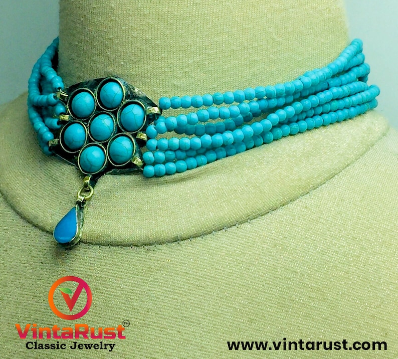 May include: A turquoise blue multi-strand beaded choker necklace with a large turquoise stone pendant. The pendant is a flower shape with a teardrop-shaped stone hanging from the center.