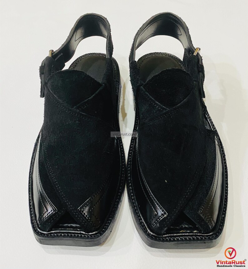 May include: A pair of black leather Peshawari sandals. The sandals feature a square toe design with a glossy finish on the toe cap and a suede upper. The sandals have an adjustable strap and buckle closure.