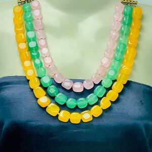 May include: A three-strand necklace with yellow, green, and pink square beads. The necklace is made of semi-precious stones and has a gold clasp.