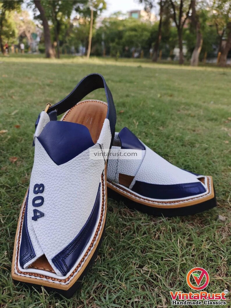 Pu&ograve; includere: Sandali in pelle bianca con dettagli blu e suola marrone. I sandali hanno una punta a punta e un cinturino che va intorno alla caviglia. I sandali hanno il numero "804" scritto su di loro.