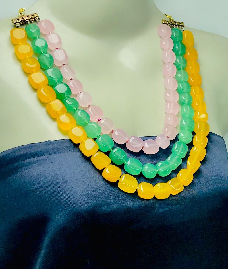 May include: A three-strand necklace with yellow, green, and pink square beads.