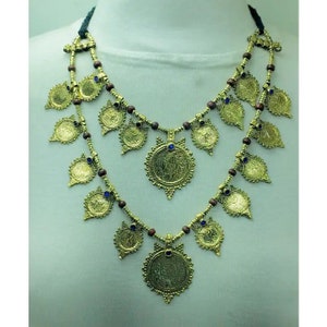 May include: A gold necklace with a double strand of brown beads and gold coin-shaped pendants. The pendants have intricate designs and blue gemstones in the centre.