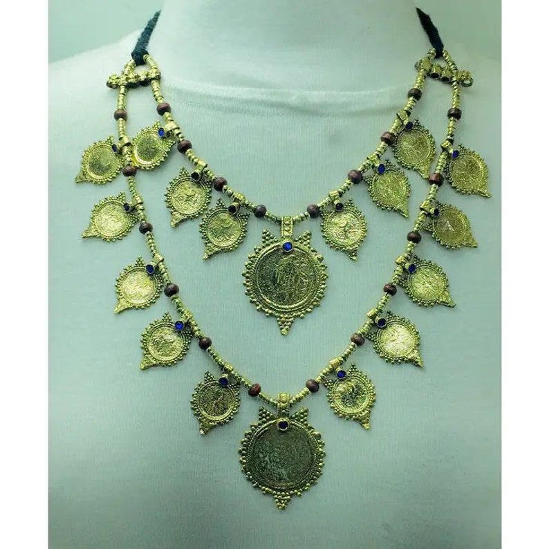 May include: A gold necklace with a double strand of brown beads and gold coin-shaped pendants. The pendants have intricate designs and blue gemstones in the centre.