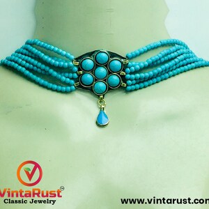 May include: A turquoise blue beaded choker necklace with a silver pendant featuring a flower design with turquoise stones. The pendant has a teardrop-shaped turquoise stone hanging from it.