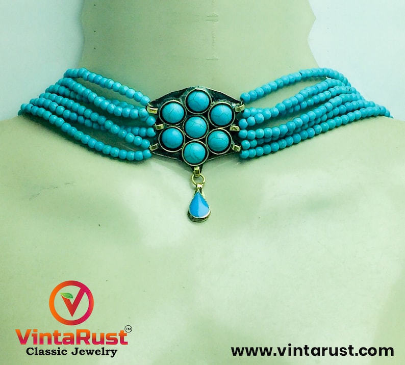 May include: A turquoise blue beaded choker necklace with a silver pendant featuring a flower design with turquoise stones. The pendant has a teardrop-shaped turquoise stone hanging from it.