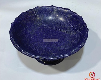 May include: A deep blue, scalloped-edge bowl made of stone. The bowl has a pedestal base and a textured surface with white veining. The bowl is a decorative item, possibly for display or serving.