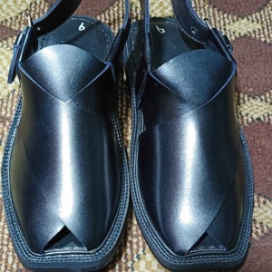 May include: A pair of black leather sandals with a strap and buckle. The sandals have a pointed toe and a thick sole.