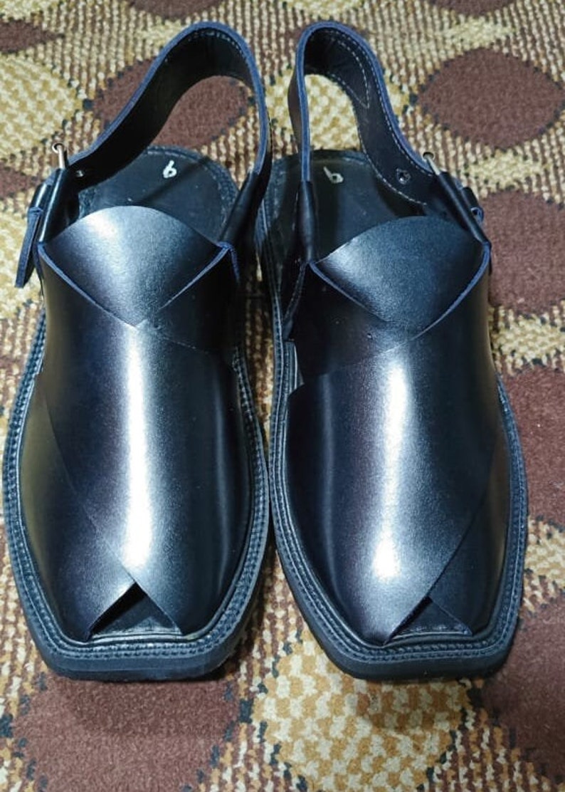 May include: A pair of black leather sandals with a strap and buckle. The sandals have a pointed toe and a thick sole.