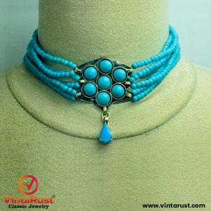 May include: A turquoise blue choker necklace with multiple strands of beads and a large pendant featuring a turquoise stone cluster. The pendant is attached to a teardrop-shaped turquoise stone.