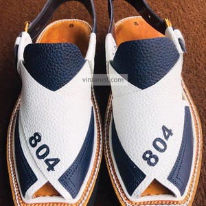 Pu&ograve; includere: Un paio di sandali in pelle bianca e blu navy con cinturino e fibbia. I sandali hanno una punta a punta e una suola spessa. Il numero "804" &egrave; stampato su ogni sandalo.