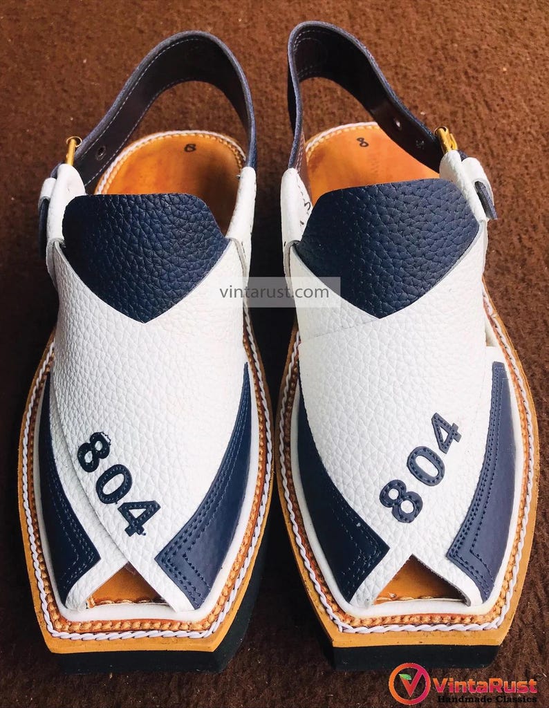 Pu&ograve; includere: Un paio di sandali in pelle bianca e blu navy con cinturino e fibbia. I sandali hanno una punta a punta e una suola spessa. Il numero "804" &egrave; stampato su ogni sandalo.