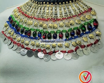 May include: A multi-layered gold and silver necklace with red, green, and blue beads. The necklace features a variety of decorative elements, including small coins and flower-shaped charms.