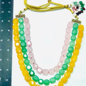 May include: A three-strand necklace with yellow, green, and pink square beads. The necklace has a gold clasp and a tassel.