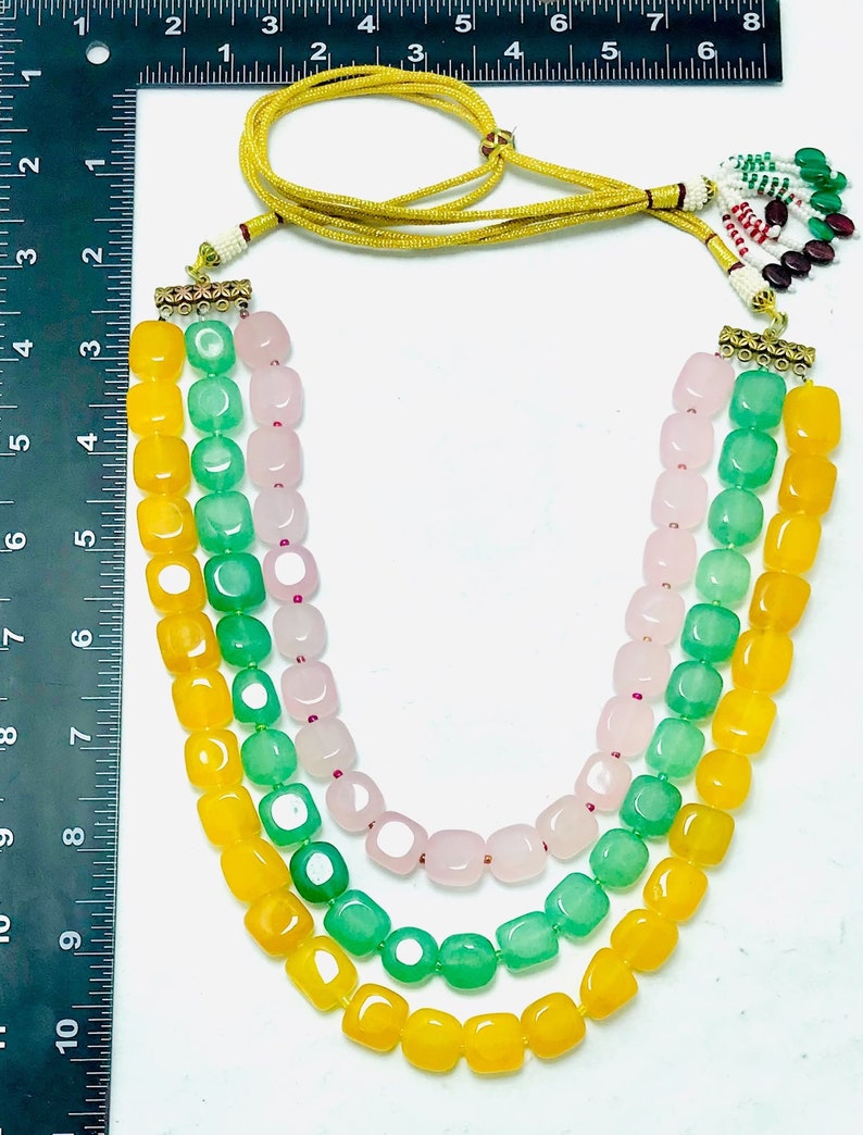 May include: A three-strand necklace with yellow, green, and pink square beads. The necklace has a gold clasp and a tassel.