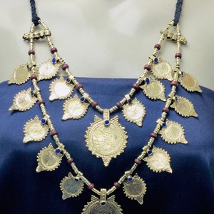 May include: A gold necklace with a double strand of wooden beads and blue glass accents. The necklace features multiple gold coin-shaped pendants.