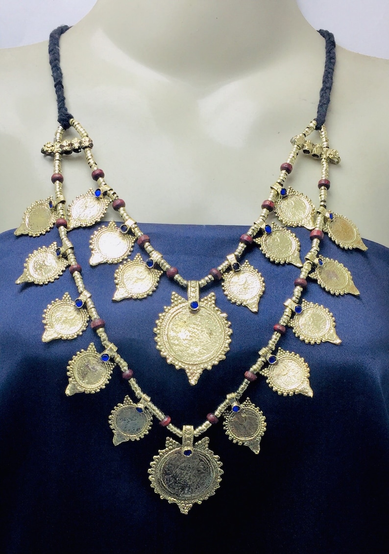 May include: A gold necklace with a double strand of wooden beads and blue glass accents. The necklace features multiple gold coin-shaped pendants.