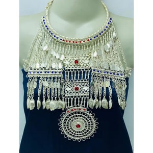 Può includere: Una collana d'argento con un grande ciondolo rotondo e una frangia di piccole perline d'argento. La collana è decorata con pietre preziose rosse e blu.