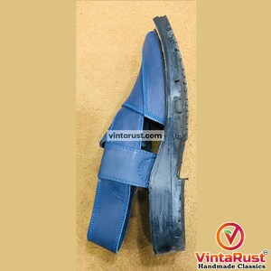 May include: Blue leather sandal with a strap and buckle closure. The sole is black and textured. The sandal has a classic design and is suitable for casual wear. The image includes the text "vintarust.com".
