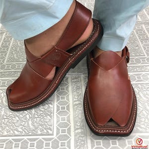 Puede incluir: Sandalias Peshawari de cuero marr&oacute;n con puntera cuadrada y detalles cosidos. Las sandalias tienen una correa en la parte superior y un cierre de hebilla. Las suelas son negras.